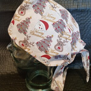 Könnte beinhalten: Weißes Weihnachts-Kopfbedeckung mit festlichem Muster. Der Stoff zeigt Rentiere, Weihnachtsbäume und Weihnachtsmannfiguren in Rot, Grau und Gold. Die Worte "Merry Christmas!" sind ebenfalls auf dem Stoff aufgedruckt.