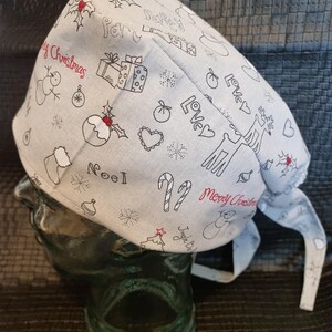 Könnte beinhalten: Eine hellgraue OP-Haube mit Weihnachtsmuster. Die Haube zeigt schwarze Strichzeichnungen von Schneemännern, Geschenken und Stechpalmen, mit roten Akzenten und den Worten "Merry Christmas".