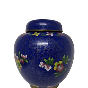 May include: A blue decorative jar with a lid, adorned with floral patterns in shades of yellow, pink, and white. The jar has a gold-colored rim and a detailed swirl design. A classic decorative piece.