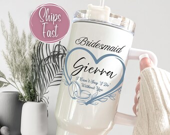 May include: White tumbler with a handle, featuring the text "Bridesmaid Sierra" inside a blue heart design. The tumbler also includes the phrase "I Can't Say 'I Do' Without You" and a ring graphic.