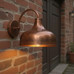 May include: A copper-colored outdoor wall-mounted light fixture. The fixture has a bell-shaped shade and a curved arm. It is mounted on a red brick wall. The light is on, casting a warm glow.