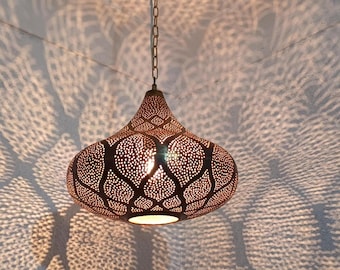 May include: A decorative pendant light with a bronze finish. The light fixture has a teardrop shape with intricate cut-out patterns that cast a patterned shadow on the wall. The light is suspended from a chain.