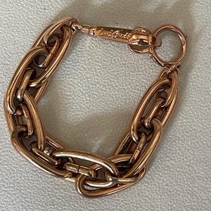 May include: A rose gold-toned chain link bracelet featuring thick, elongated oval links. The bracelet includes a lobster claw clasp mechanism with an engraved signature logo and a circular jump ring for secure fastening.