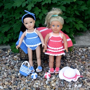 May include: Two dolls wearing crocheted swimsuits, one in blue and one in pink, with matching beach accessories including a striped bag, a sun hat, and beach balls.