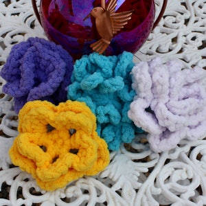 May include: Four colorful, chunky knit yarn balls in shades of purple, teal, yellow, and lavender. The yarn balls are arranged on a white, ornate table. A hummingbird feeder is visible in the background.