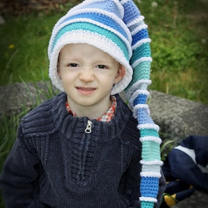 May include: A young boy wearing a blue and white striped crocheted hat with a long tail. He is wearing a dark blue sweater and jeans.