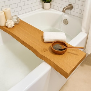 Puede incluir: Una bandeja de baño de madera con borde natural, que sostiene un pequeño cuenco de madera con una cuchara, una toalla blanca, velas y un objeto decorativo. La bandeja es de madera marrón claro y abarca el ancho de la bañera.