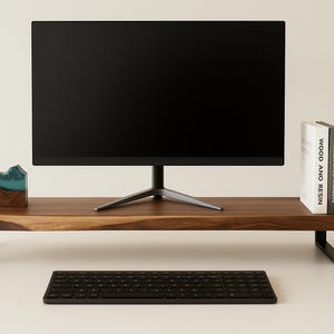May include: A wooden monitor stand with black legs, a black keyboard, and a black monitor. The stand has a natural wood grain finish. A small decorative item with blue resin accents and a book titled "WOOD AND RESIN" are on the stand.