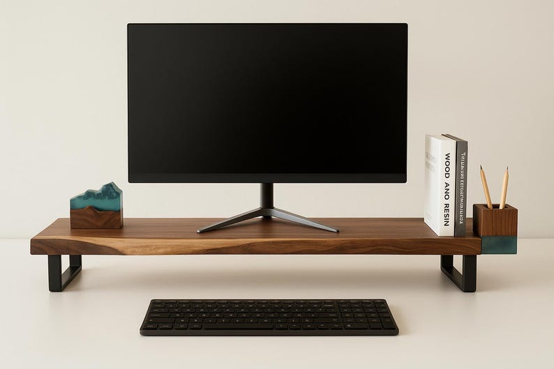 May include: A wooden monitor stand with black legs, a black keyboard, and a black monitor. The stand has a natural wood grain finish. A small decorative item with blue resin accents and a book titled "WOOD AND RESIN" are on the stand.