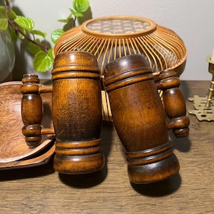 May include: Two vintage wooden beer steins with handles. The steins are made of dark brown wood and have a classic, cylindrical shape with a decorative band around the middle. The handles are also made of wood and are attached to the side of the steins.