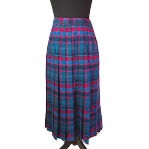 May include: A pleated midi skirt in a plaid pattern of teal, blue, and magenta. The skirt is displayed on a black mannequin. The plaid design features vertical and horizontal lines creating a grid-like pattern.