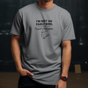 May include: A gray t-shirt with the text "I'M NOT AN EARLY BIRD. or a night owl. I'm just a tired pigeon." in black. A cartoon drawing of a pigeon is below the text.