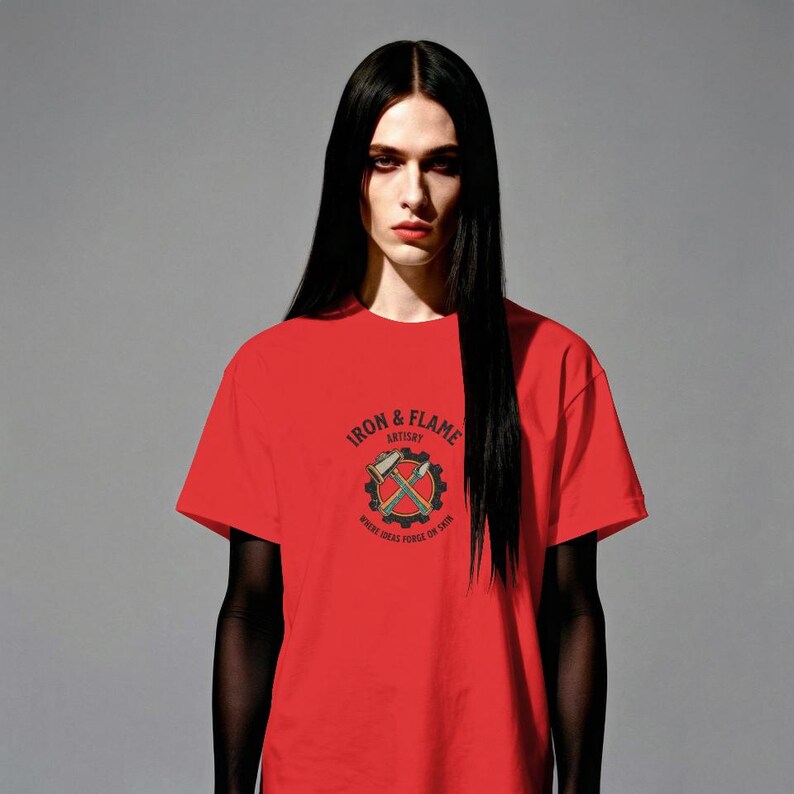 K&ouml;nnte beinhalten: Ein rotes T-Shirt mit dem Text "IRON & FLAME ARTISTRY" und einer Grafik von gekreuzten Werkzeugen in einem Zahnrad. Das T-Shirt ist kurz&auml;rmlig und hat einen Rundhalsausschnitt. Das Model hat lange schwarze Haare.
