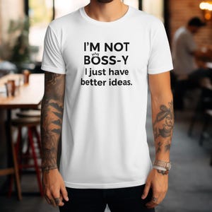 May include: White t-shirt with the text "I'M NOT BOSS-Y I just have better ideas." in black. The shirt has a crew neck and short sleeves. The text includes a small crown graphic above the letter "Y".