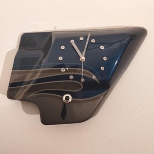 May include: A blue and black motorcycle part clock with silver accents. The clock face has silver hands and silver hour markers.