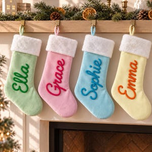Puede incluir: Cuatro calcetines navideños suaves en colores pastel: verde claro, rosa, azul claro y amarillo pálido. Cada calcetín tiene un puño de felpa blanca y un lazo para colgar. Los nombres Ella, Grace, Sophie y Emma están bordados en colores a juego.