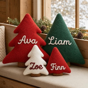 May include: Four plush, textured Christmas tree-shaped pillows with brown bases. A large red tree features the white embroidered name Ava, a large green tree features the white name Liam, a small white tree features the red name Zoe, and a small red tree features the white name Finn.