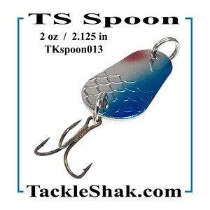 May include: A fishing lure with a silver, blue, and red design. The lure is 2.125 inches long and weighs 2 oz. The text "TS Spoon" and "TackleShak.com" are visible. The lure has two hooks and is designed for trout, bass, and pan fish.