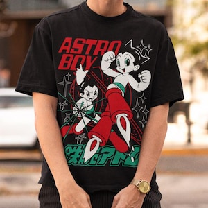 May include: Black t-shirt with a graphic of Astro Boy in red, white, and green. The text "ASTRO BOY" is in red, with Japanese characters below the illustration. The shirt is short-sleeved.