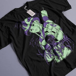 May include: Black t-shirt featuring a graphic illustration of a green and purple figure with a stylized design. The design includes a face, a sphere, and lightning bolt shapes. A white tag is attached to the shirt.