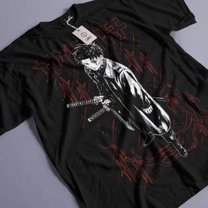 May include: Black t-shirt featuring a detailed anime-style illustration in red and white. The graphic depicts a character with swords, set against a backdrop of Japanese text and abstract lines. A tag is attached to the shirt.