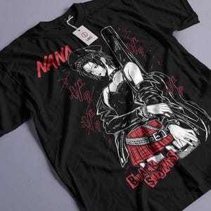 May include: Black t-shirt featuring a manga-style illustration of a woman with a guitar case. The design includes the text "NANA" in red, along with "Black Stones". The shirt has a tag that says "LARGE".