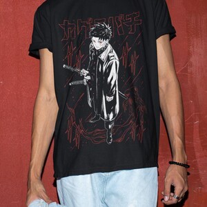 May include: Black t-shirt featuring a red and white anime-style illustration of a character holding two swords. The graphic includes Japanese text at the top. The character is wearing a long coat and has red eyes. The shirt is a crew neck.
