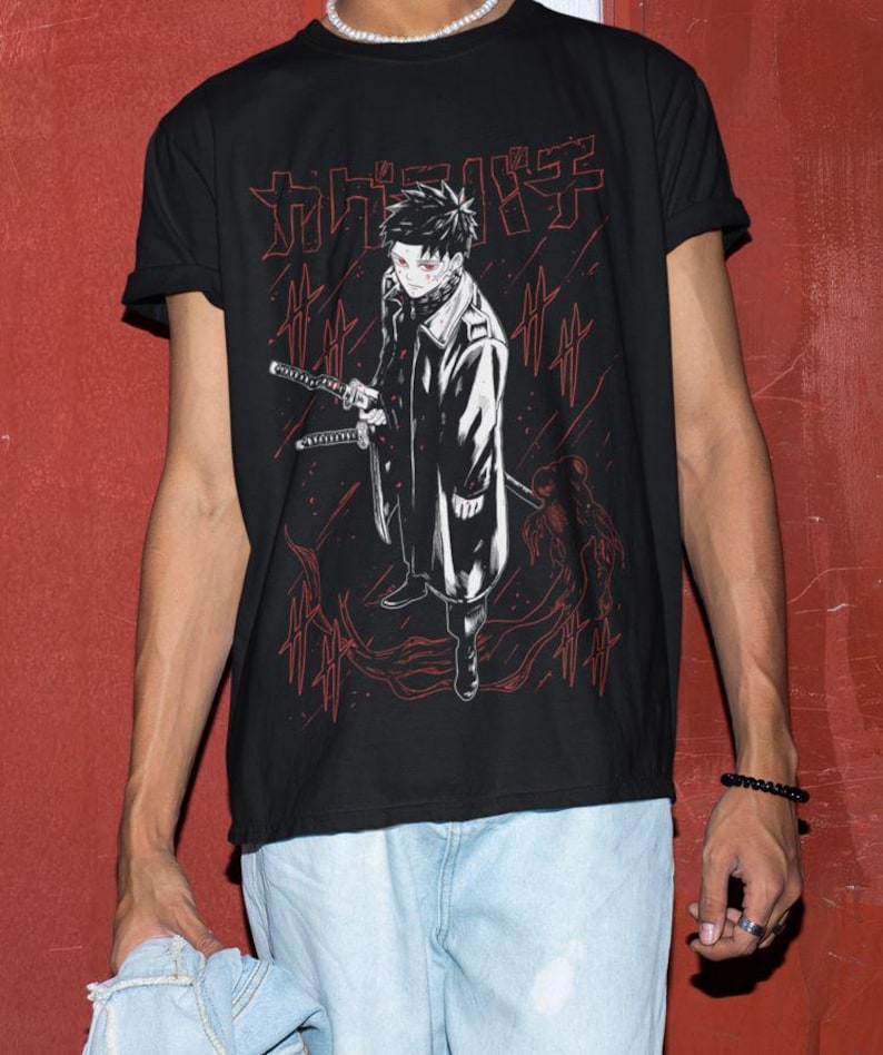 May include: Black t-shirt featuring a red and white anime-style illustration of a character holding two swords. The graphic includes Japanese text at the top. The character is wearing a long coat and has red eyes. The shirt is a crew neck.