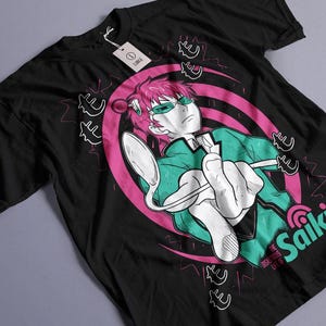 May include: Black t-shirt featuring a graphic of an anime character with pink hair, green glasses, and a green jacket holding a spoon. The design includes pink and white accents and the word "Saiki".