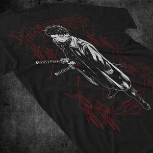 May include: Black t-shirt featuring a manga-style illustration of a character with red eyes and a long coat, holding two swords. Red Japanese text and graphic elements are scattered around the character, creating a dynamic design.