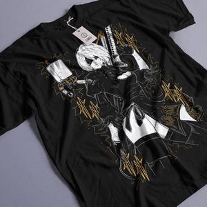 May include: Black t-shirt featuring a detailed illustration of a female anime character with white hair, holding a weapon. The design includes gold accents and a tag. The shirt is made of a soft material.