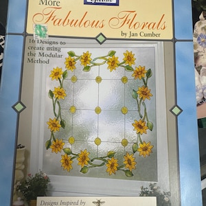 May include: A book cover titled "More Fabulous Florals" by Jan Cumber. The cover features a stained glass design with yellow sunflowers and green leaves. The text "16 Designs to create using the Modular Method" is also visible.