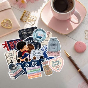 Peut inclure: Une collection d'autocollants en vinyle avec des illustrations sur le thème du hockey, incluant un couple qui s'embrasse, un sweat à capuche gris avec le texte Briar University, une pile de livres, une tasse de café et des motifs en forme de cœur.