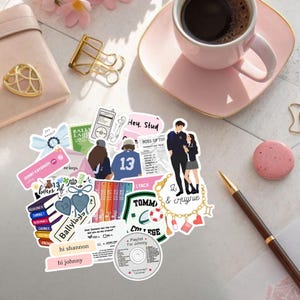 May include: A collection of assorted stickers featuring various illustrations, including a couple, books, a music player, a charm bracelet, and text elements like "Hey. Stud," "hi shannon," "hi johnny," "Ballylaggan," and "Playlist For Johnny."