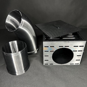 May include: An assortment of metallic components, including a curved pipe, a cylindrical piece, and a square box with a carbon fiber lid. The box has a large circular opening and several rectangular cutouts.