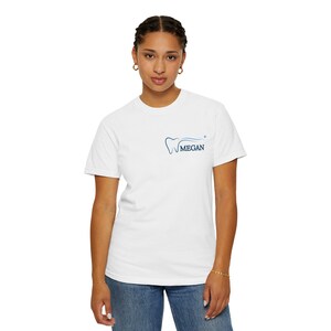 Peut inclure: Un t-shirt blanc à manches courtes avec un petit motif sur la poitrine gauche. Le motif se compose d'un contour de dent bleu, d'une ligne courbe bleue, d'une petite étoile bleue et du nom MEGAN imprimé en lettres capitales bleues.