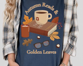 May include: A navy blue t-shirt featuring a graphic of a beige mug of tea, a brown book titled "FAV POETRY," a lit candle, eyeglasses, and scattered autumn leaves with the text "Autumn Reads & Golden Leaves" printed in a light orange font.
