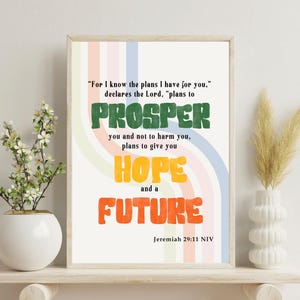 May include: Framed print with the words "PROSPER, HOPE, and FUTURE" in bold, colorful letters. The text is set against a pastel rainbow background. The quote is from Jeremiah 29:11 NIV.