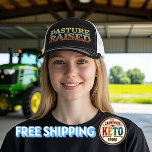May include: Black and white trucker hat with the text "PASTURE RAISED" in a retro font. The hat is worn by a person in front of a tractor. The shirt says "FREE SHIPPING" and has a "The Carnivore Keto Store" logo.