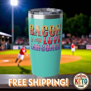 以下が含まれることがあります： 銀色の縁と蓋が付いた、ターコイズ色の断熱タンブラー。「BACON is my LOVE LANGUAGE」というテキストがレトロなフォントで表示されています。背景には野球場が写っています。