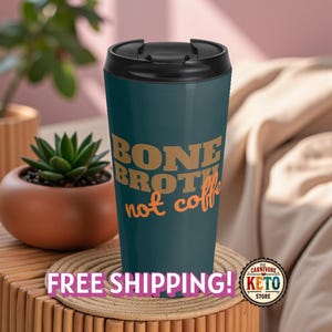 以下が含まれることがあります： 黒い蓋が付いた、レトロなフォントで「BONE BROTH not coffee」と書かれた、ティール色のトラベルマグ。マグカップは木製の表面に置かれ、背景には植物があります。「Carnivore Keto Store」のロゴが見えます。