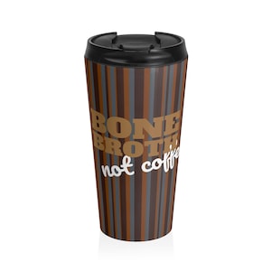 Op de afbeelding: Een reismok met een zwart deksel en een bruin, grijs en blauw gestreept patroon. De mok heeft de tekst "BONE BROTH, not coffee" in een vet, gestileerd lettertype, wat een drankalternatief suggereert.