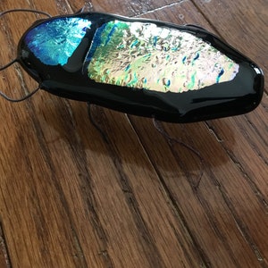 May include: A black glass beetle with iridescent blue and gold wings. The beetle is a decorative object and has a wire antenna.