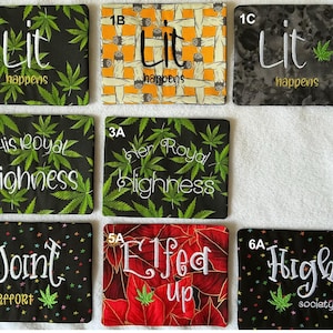 May include: A collection of eight rectangular fabric pouches featuring embroidered text and patterns. Designs include green cannabis leaves, rolled cigarettes, and floral motifs with phrases like Lit happens, His Royal Highness, Joint effort, and High society.