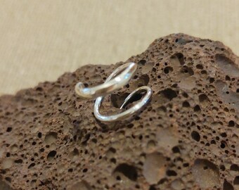 May include: A silver, twisted, open ring, designed to be worn on the ear. The ring is shown on a brown, textured surface.