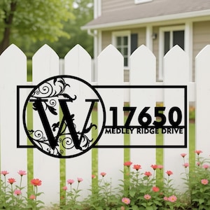 May include: A black metal address sign featuring a large letter W inside a circular frame with decorative scrollwork. To the right of the circle, the number 17650 is displayed above the text MEDLEY RIDGE DRIVE, all enclosed in a rectangular frame.