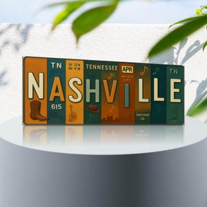 May include: A rectangular metal sign featuring the word "NASHVILLE" in large, stylized letters. The sign includes images of a cowboy boot, guitar, and a hat. The sign also includes the text "TENNESSEE" and "APR MUSIC CITY".