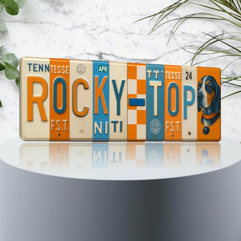 K&ouml;nnte beinhalten: Rechteckiges Metallschild mit den Worten "ROCKY TOP" in orangefarbenen und blauen Blockbuchstaben. Das Schild hat einen cremefarbenen Hintergrund mit orangefarbenen und blauen Akzenten. Auf der rechten Seite des Schildes befindet sich eine Illustration eines Jagdhundes.