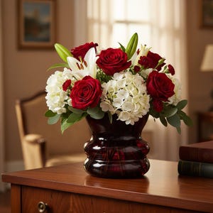 Puede incluir: Un arreglo floral con rosas rojas vibrantes, lirios blancos e hortensias en un jarrón rojo oscuro. El ramo se coloca sobre una superficie de madera, creando una exhibición clásica y elegante. Las flores son frescas y en plena floración.