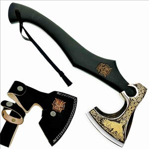 May include: A black axe with a wooden handle and a decorative blade featuring gold-colored engravings. The axe includes a black leather sheath and a wrist strap. The blade has a gold-colored design of a bird.